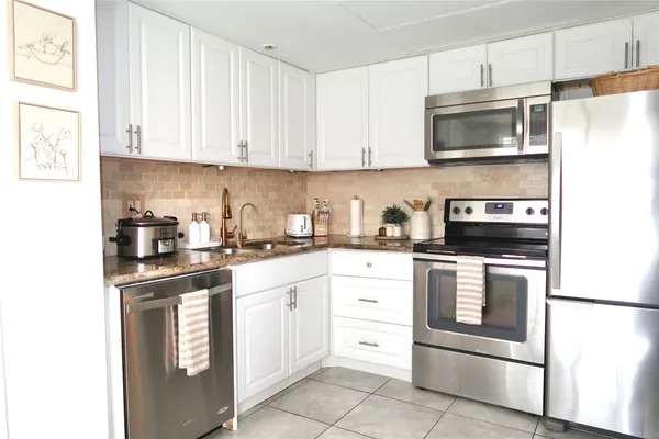a kitchen with stainless steel appliances granite countertop a refrigerator stove a sink and white cabinets