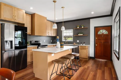 a kitchen with stainless steel appliances granite countertop a refrigerator a sink dishwasher a stove and white cabinets with wooden floor