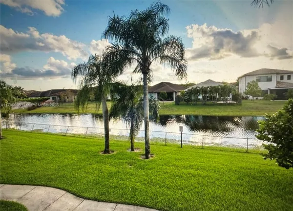 a view of lake with a big yard and palm trees