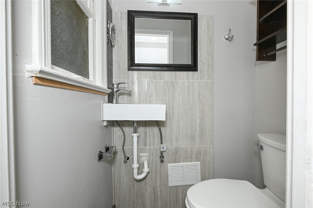 3699 Bainbridge Road Cleveland Heights, OH 44118 - Photo 18 of 37 Compact powder room featuring a wall-mounted sink with chrome faucet, a framed mirror, and vertical tiled accent wall
