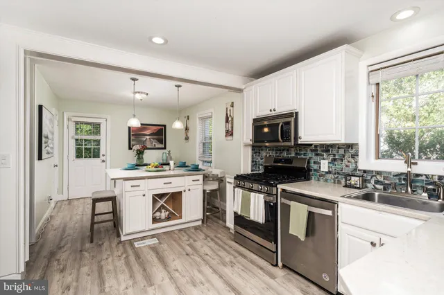 a kitchen with stainless steel appliances granite countertop a stove top oven a sink dishwasher a refrigerator and white cabinets with wooden floor