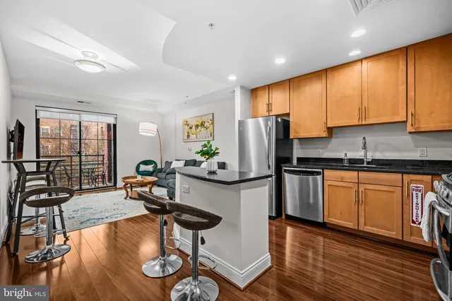 a kitchen with stainless steel appliances granite countertop a refrigerator a stove a sink a dining table and chairs with wooden floor