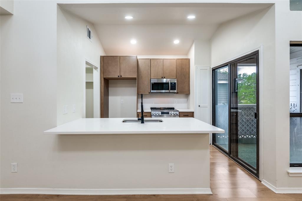 17490 Meandering Way, Unit 2202 Dallas, TX 75252 - Photo 13 of 24 Kitchen featuring a breakfast bar with white countertop, stainless steel appliances, wood-finish flooring, and sliding glass doors to exterior