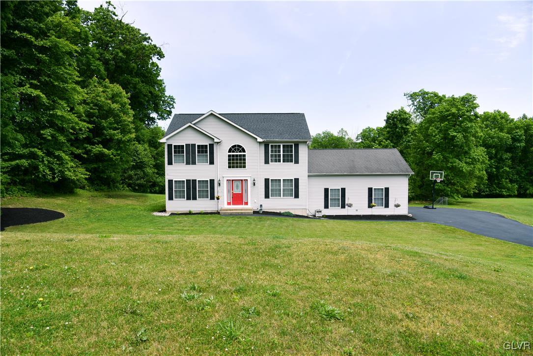 a white house with a big yard and large trees with wooden fence
