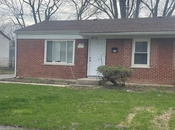 a brick house that has a small yard and large trees