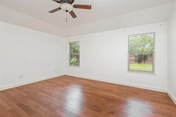 an empty room with wooden floor chandelier fan and windows