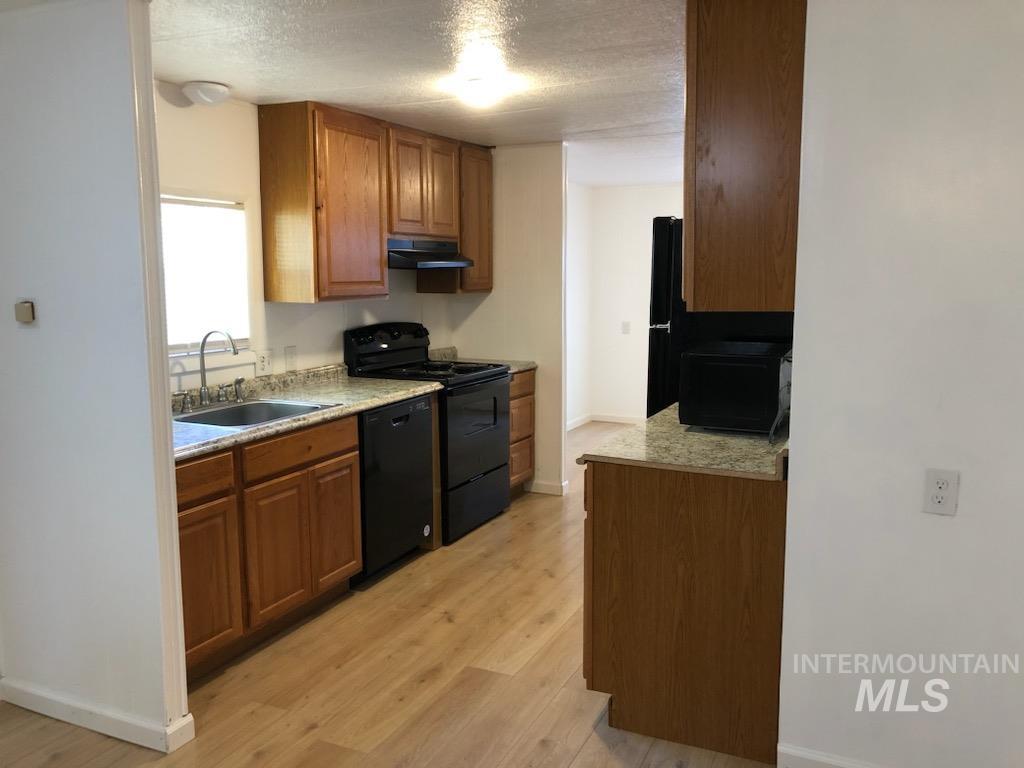 655 Dolson Lane Eagle, ID 83616 - Photo 7 of 23 Kitchen featuring wood finish cabinetry, black appliances, light wood-style floors, a textured ceiling, and light stone countertops