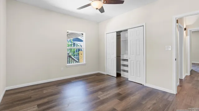 an empty room with wooden floor chandelier fan and windows