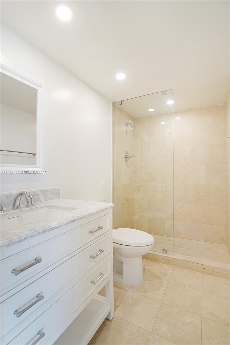 5101 Collins Avenue, Unit 14R Miami Beach, FL 33140 - Photo 7 of 9 a bathroom with a granite countertop sink a toilet a mirror and shower