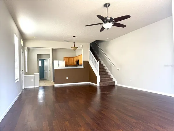 a view of an empty room with wooden floor and a ceiling fan
