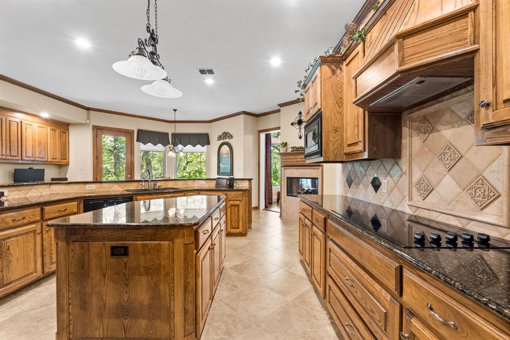 10072 Bluffview Circle Pilot Point, TX 76258 - Photo 18 of 38 Kitchen with backsplash, dark stone counters, brown cabinetry, crown molding, and hanging light fixtures