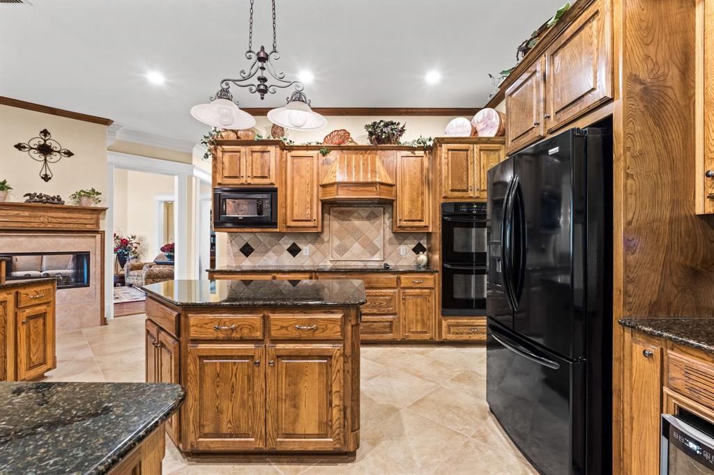 10072 Bluffview Circle Pilot Point, TX 76258 - Photo 19 of 38 Kitchen featuring brown cabinetry, dark stone counters, black appliances, backsplash, and hanging light fixtures