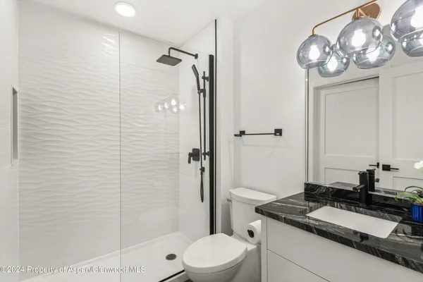 a bathroom with a granite countertop sink a toilet a mirror and shower