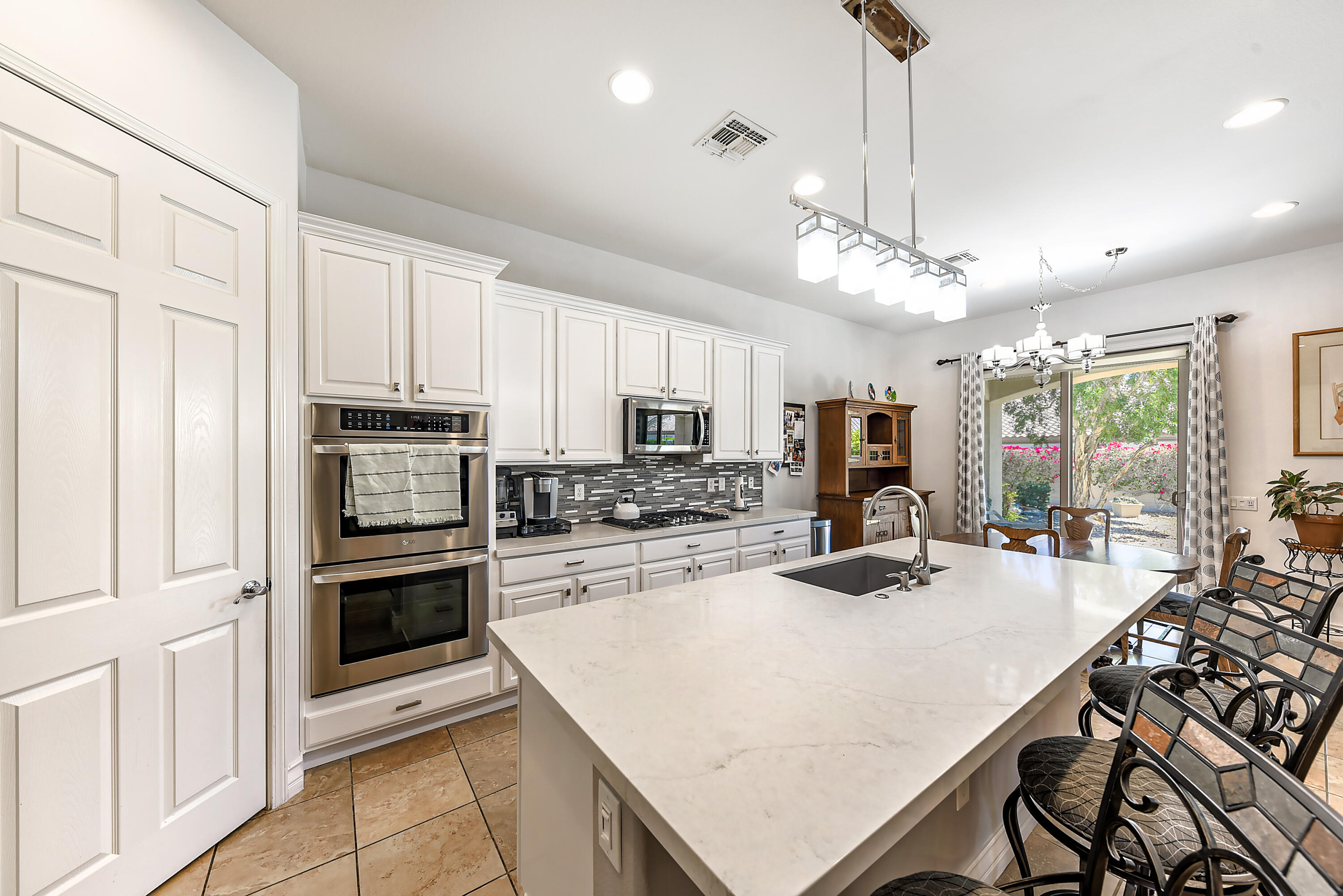 a kitchen with stainless steel appliances kitchen island granite countertop a stove a sink a microwave a dining table and chairs with white cabinets