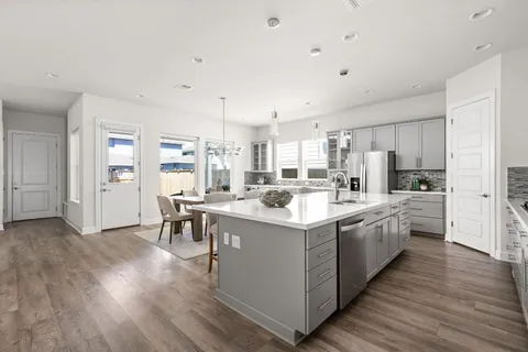 a large kitchen with stainless steel appliances a stove top oven a refrigerator a sink dishwasher and a dining table with wooden floor