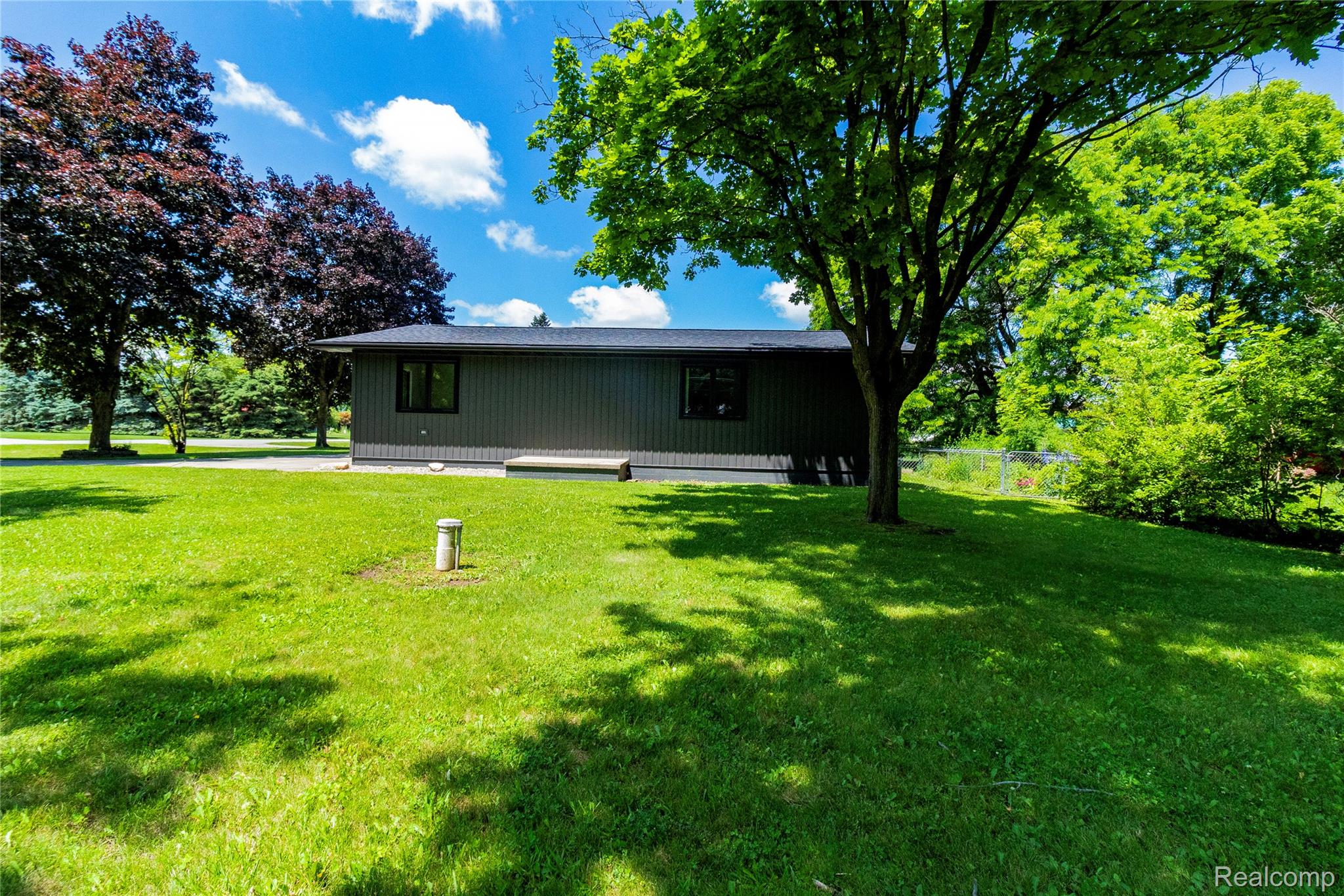1138 Baldwin Road Lapeer, MI 48446 - Photo 48 of 49 Expansive green lawn with mature trees and a single-story structure featuring dark siding and black-framed windows