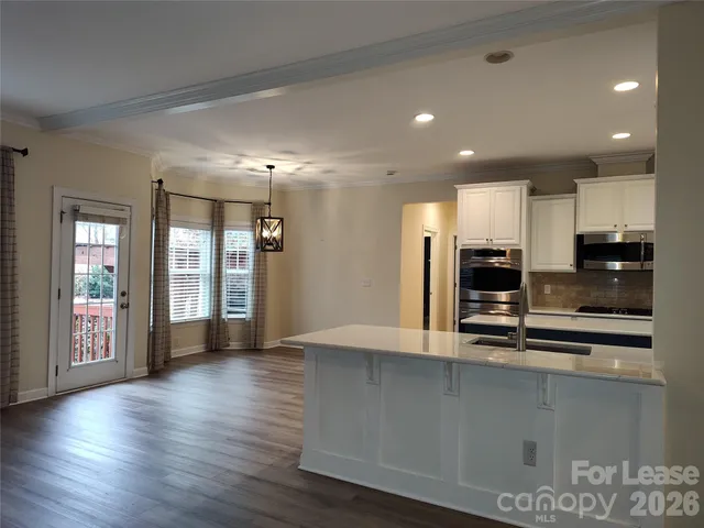 a view of kitchen with stainless steel appliances granite countertop a large counter top and wooden floors