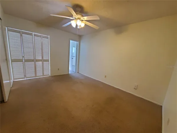 an empty room with a chandelier fan and windows
