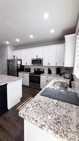 a large kitchen with kitchen island granite countertop a stove a sink a refrigerator and white cabinets