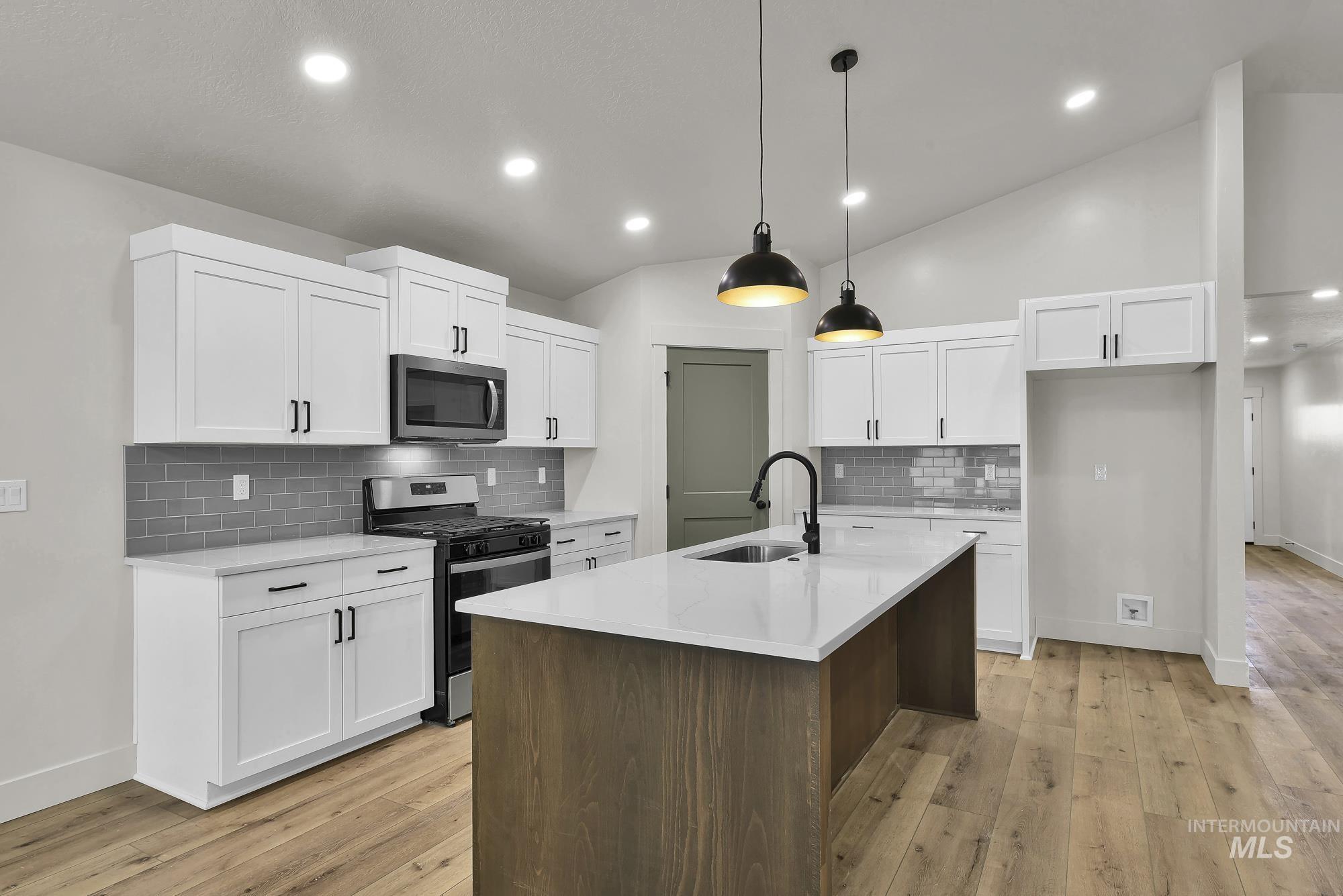 1130 Velvet Loop Wilder, ID 83676 - Photo 11 of 35 Kitchen featuring white shaker cabinetry, an island with a built-in sink, gray subway tile backsplash, stainless steel appliances, and wood-finish flooring