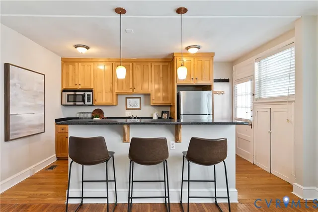 a kitchen with stainless steel appliances granite countertop a stove a refrigerator a sink a dining table and chairs with wooden floor