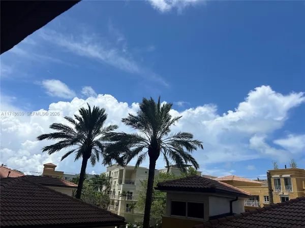 a view of a palm tree with flower plants and wooden fence