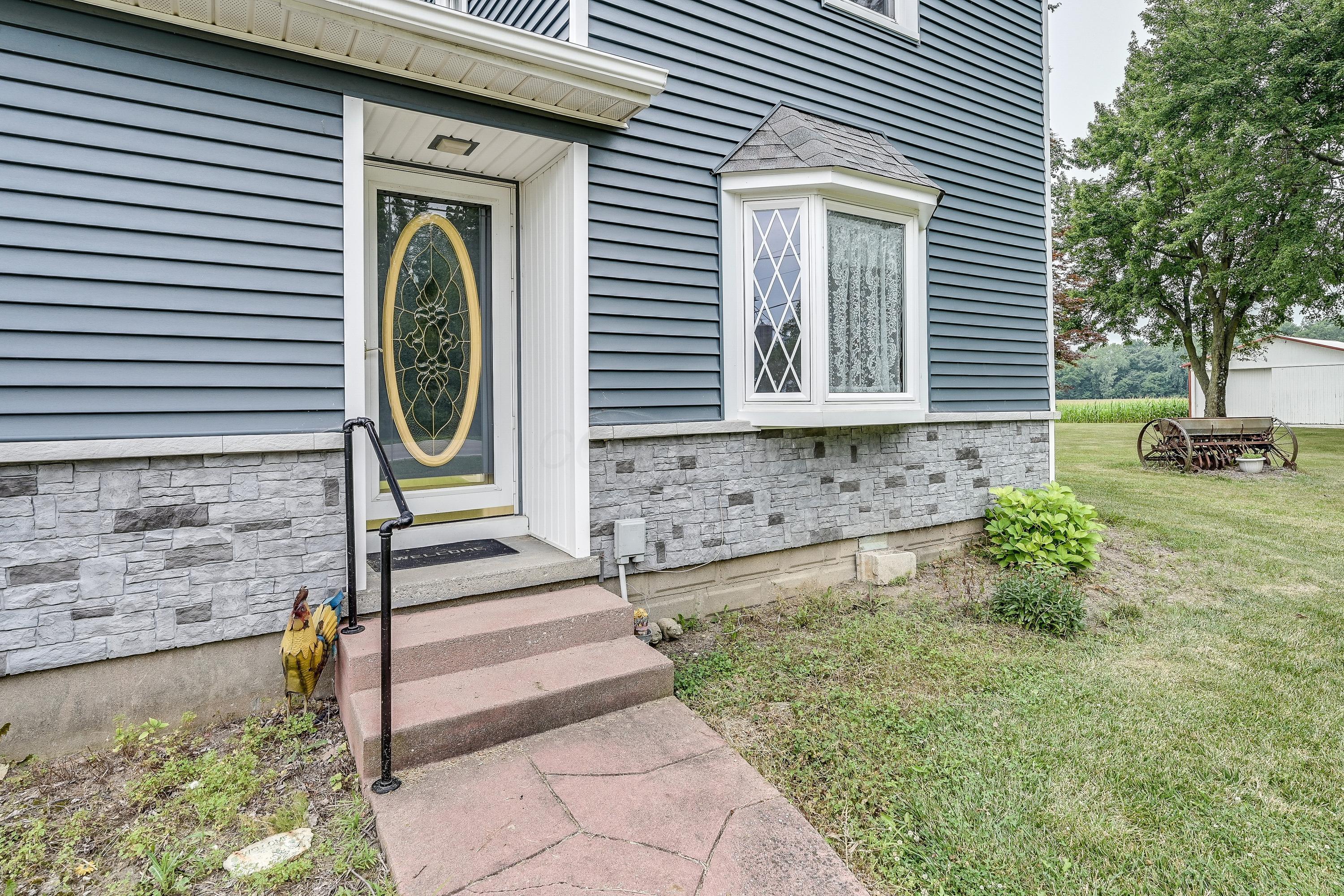 19834 Botkins Road Jackson Center, OH 45334 - Photo 2 of 32 Exterior featuring blue horizontal siding, a stone veneer foundation, and a decorative glass entry door