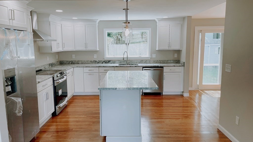 a kitchen with kitchen island granite countertop wooden floors and white cabinets