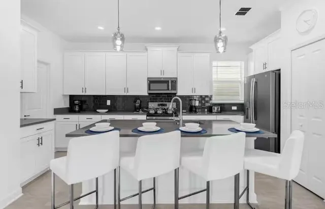 a kitchen with stainless steel appliances granite countertop a sink a stove a refrigerator cabinets and chairs