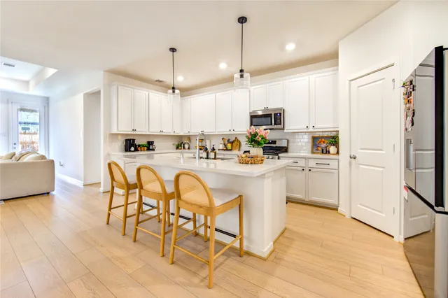 a kitchen with stainless steel appliances kitchen island granite countertop a stove a sink a refrigerator and white cabinets with wooden floor