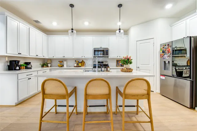 a kitchen with stainless steel appliances granite countertop a dining table chairs sink refrigerator and microwave