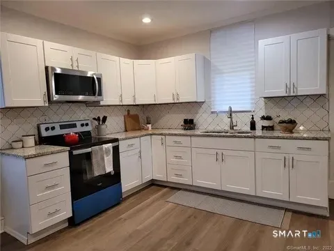 a kitchen with stainless steel appliances granite countertop a stove a sink dishwasher and a microwave oven with white cabinets