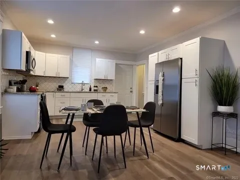 a kitchen with stainless steel appliances kitchen island granite countertop a dining table chairs and a refrigerator