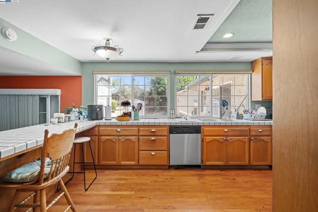 a kitchen with stainless steel appliances granite countertop a stove a sink dishwasher and a dining table with wooden floor