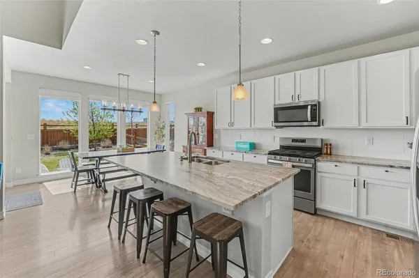 a kitchen with stainless steel appliances granite countertop a stove a sink a microwave a dining table and chairs with wooden floor