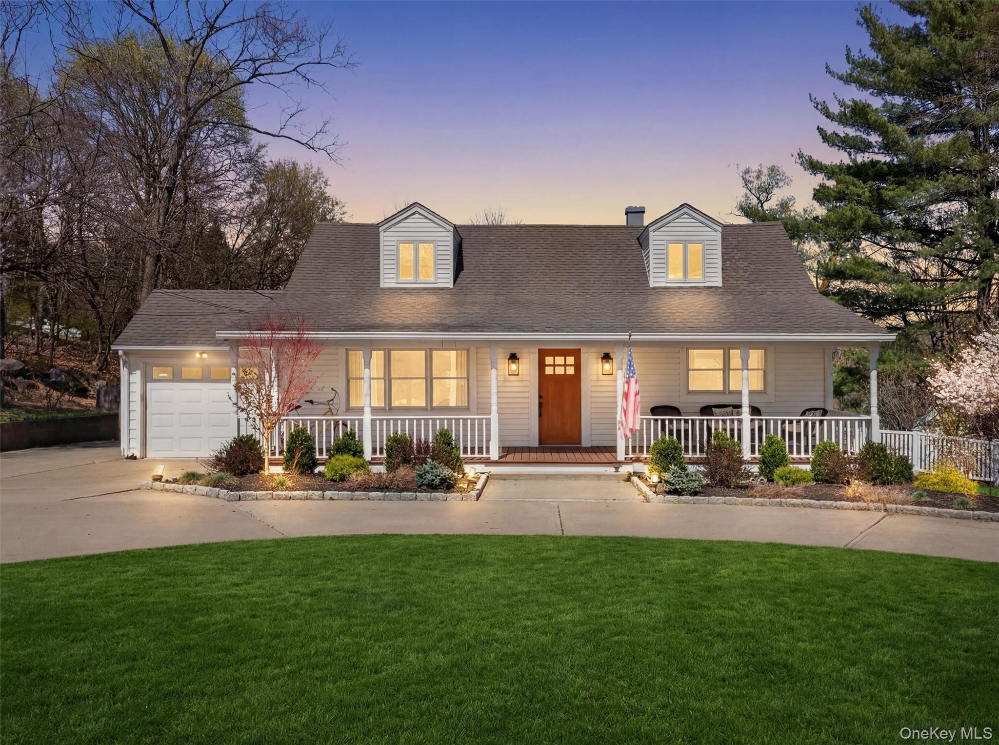 Cape cod-style house with covered porch, roof with shingles, an attached garage, a yard, and driveway