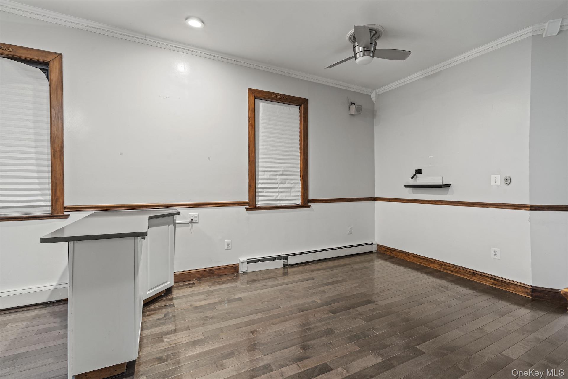 Spare room featuring ornamental molding, a ceiling fan, a baseboard radiator, and dark wood-type flooring