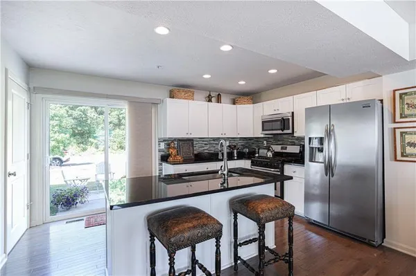 a kitchen with stainless steel appliances granite countertop a refrigerator a stove a sink dishwasher and white cabinets with wooden floor