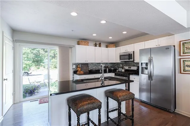 a kitchen with stainless steel appliances granite countertop a refrigerator a stove a sink dishwasher and white cabinets with wooden floor