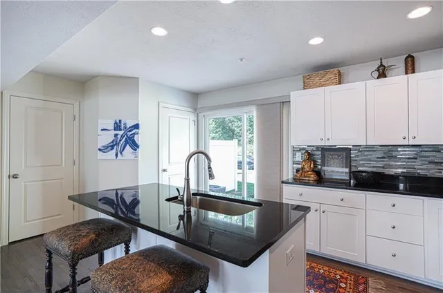 a kitchen with granite countertop a stove a sink a refrigerator and white cabinets with wooden floor