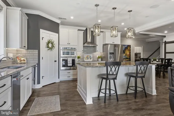 a kitchen with stainless steel appliances kitchen island granite countertop a refrigerator a stove and white cabinets with wooden floor