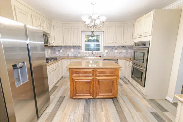 a kitchen with stainless steel appliances granite countertop a refrigerator a sink a stove and white cabinets with wooden floor