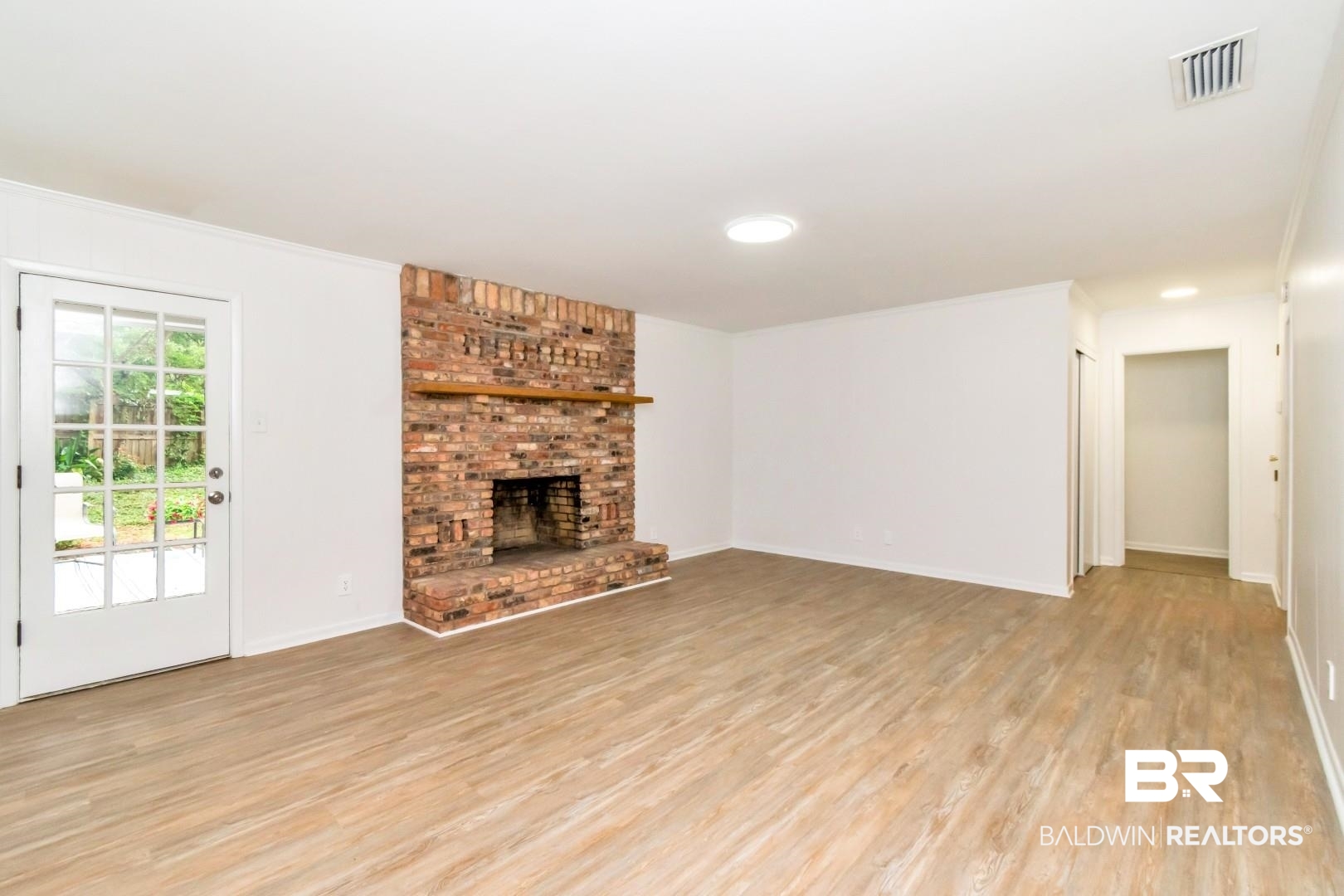 5217 Perin Road Mobile, AL 36693 - Photo 24 of 45 Spacious living area featuring a brick-front fireplace with a wood mantel, wood-finish flooring, and a glass-paneled door opening to the exterior