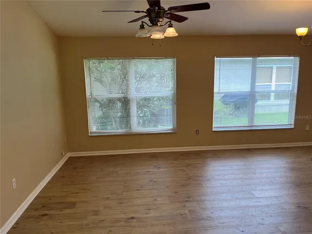 an empty room with wooden floor fan and windows