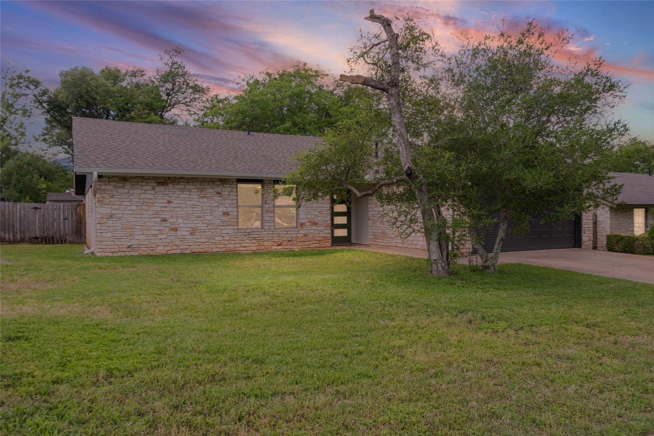 A classic ranch home, clad in stone, awaits with a broad driveway and mature trees.