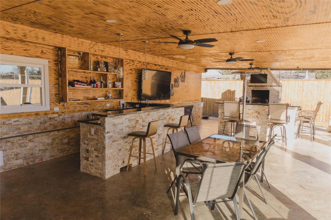 918 Fresa Road Pasadena, TX 77502 - Photo 20 of 47 spacious outdoor entertainment area with a wooden ceiling, ceiling fans, and stone accents. It features a large bar, ample seating, a flat-screen TV, and an outdoor kitchen with a grill, offering an ideal space for hosting gatherings.