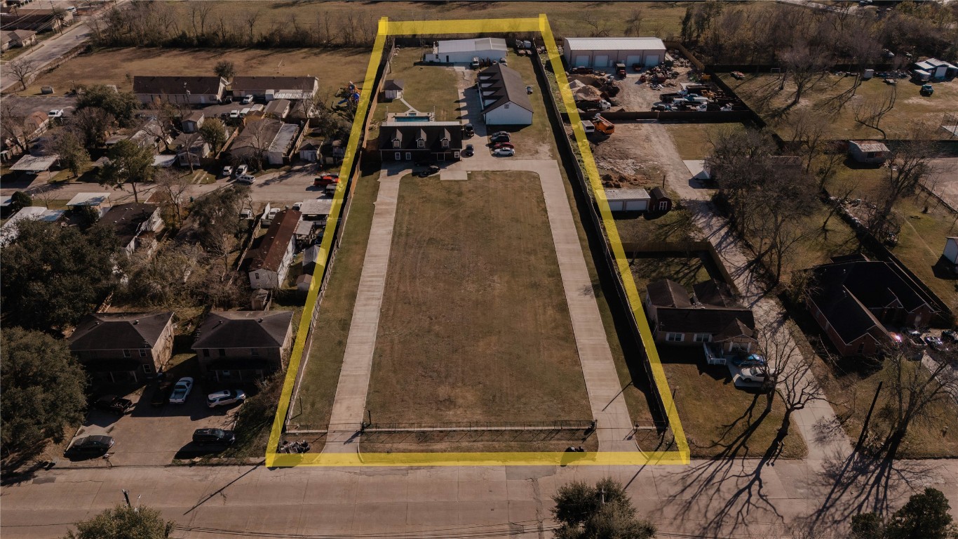 918 Fresa Road Pasadena, TX 77502 - Photo 2 of 47 This aerial photo showcases a long rectangular property outlined in yellow. It features a large driveway leading to a main house and multiple outbuildings, surrounded by open land. The property is set in a residential area with neighboring homes.