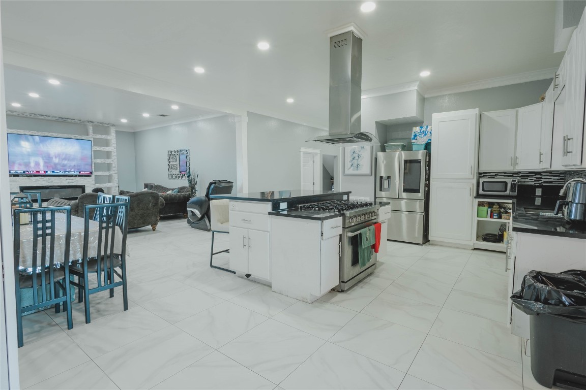 918 Fresa Road Pasadena, TX 77502 - Photo 8 of 47 This open-concept kitchen and living area features modern appliances, sleek white cabinetry, and a large island with a cooktop. The space flows into a cozy living room with a wall-mounted TV, creating an inviting atmosphere for entertaining.