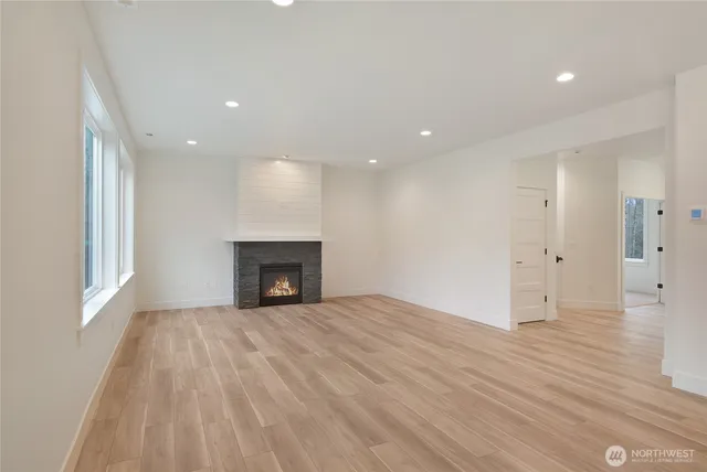 a view of an empty room with wooden floor fireplace and a window