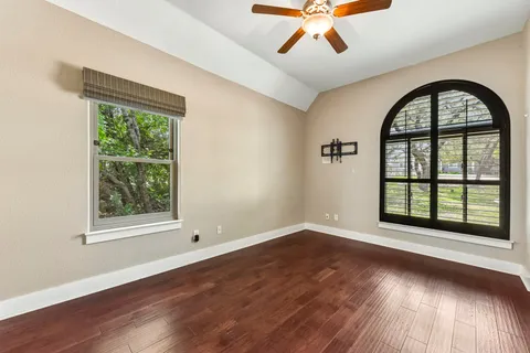 an empty room with wooden floor windows and a ceiling fan